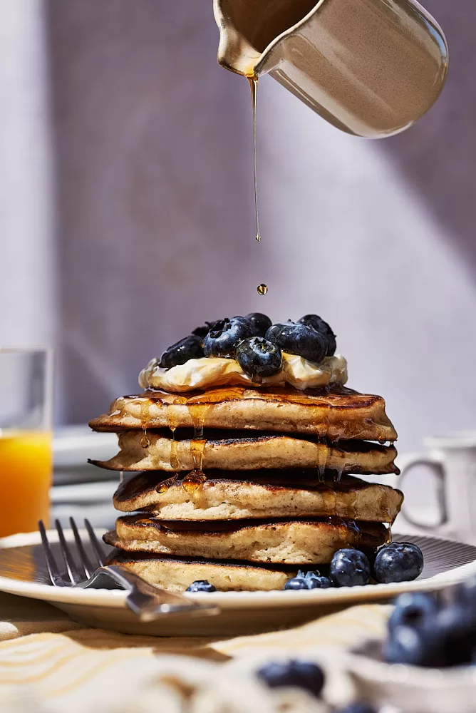 Food photography in Barcelona of blueberry cream cheese pancakes with action of pouring syrup