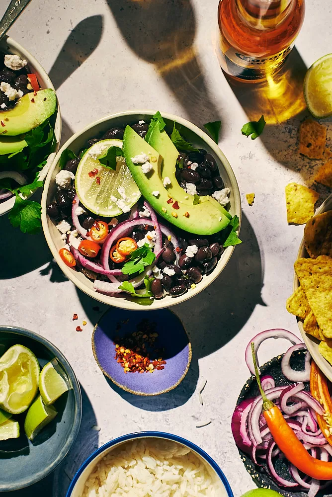 Food photography of Mexican food feast of black bean bowls with lime, avocado, chilis, and nachos