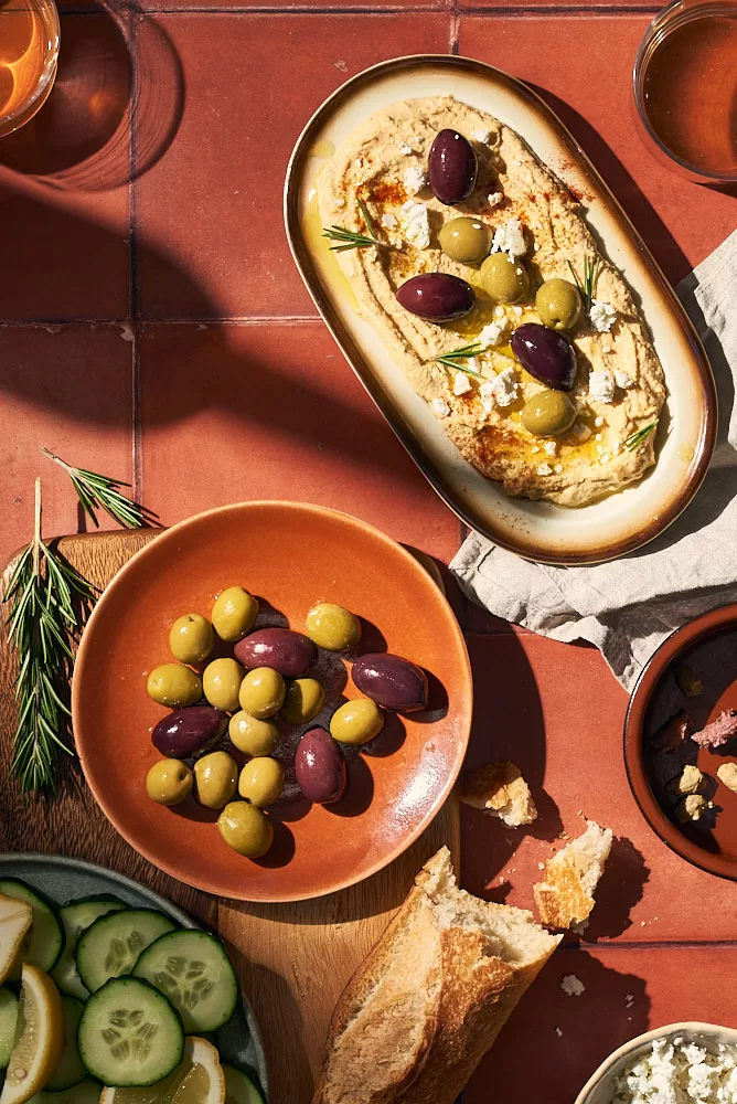 Mediterranean summer scene in hard light of hummus, bread and olives on a terracotta title background